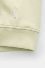 Close-up view of the hem and fabric texture of the 04651/ A trip in a bag Sweatjacke 'CL Bomber' pastellgrün, showing soft ribbed cuffs and a small white brand label. Entspannt unterwegs: Die Sweatjacke 'CL Bomber' von 04651/ A TRIP IN A BAG kombiniert ei