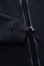 Nahaufnahme der Stone Island Sweatjacke 'Ghost Piece' navy aus elastischer Baumwolle mit Reißverschluss, Rippbündchen und tonalem Kompass-Badge, Perspektive frontal auf Ärmel und Mittelfront.