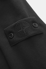 Nahaufnahme der Stone Island Sweatjacke 'Ghost Piece' schwarz, Perspektive von der Ärmelinnenseite auf das tonale Kompass-Badge mit Knöpfen.