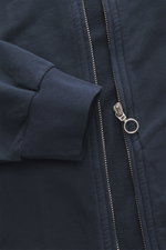Nahaufnahme der 04651/ A trip in a bag Sweatjacke 'IF Track' navy, von oben fotografiert, zeigt Reißverschluss, elastisches Rippbündchen, Baumwoll-Jersey, garment-dyed, Regular Fit, schräge Leistentaschen, hochschließenden Kragen und kleines Weblabel.