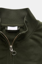 Nahaufnahme der dunkelgrünen 04651/ A trip in a bag Sweatjacke 'IF Track' aus Baumwoll-Jersey mit Reißverschluss, hoch geschlossenem Kragen und kleinem Weblabel, fotografiert von oben.