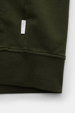 Nahaufnahme der dunkelgrünen 04651/ A trip in a bag Sweatjacke 'IF Track' von unten, zeigt super soften Baumwoll-Jersey mit elastischen Rippbündchen und kleinem Weblabel.