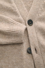 Nahaufnahme aus schräger Perspektive des 04651/ A trip in a bag Cardigan 'Hunter' taupe meliert mit grobem Strickbild, V-Ausschnitt, Vier-Knopf-Leiste, aufgesetzten Fronttaschen, komfortablen Rippbündchen, Regular Fit, weichem Griff und Mix aus Merinowoll