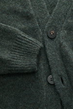 Nahaufnahme aus leichter Schräge des dunkelgrün melierten 04651/ A trip in a bag Cardigan 'Hunter' mit grobem Strickbild, V-Ausschnitt, Vier-Knopf-Leiste, aufgesetzten Taschen, Rippbündchen, Regular Fit, weichem Griff, Mix aus Merinowolle und Microfaser.