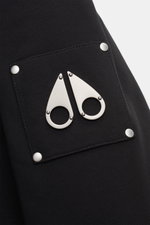 Nahaufnahme der schwarzen Moose Knuckles Sweatjacke 'Classic Bunny' mit Metall-Logo auf der Kängurutasche, Jersey aus Baumwolle, Slim Fit, leichte Wattierung, Kapuze mit Faux-Fur-Innenfutter, robuste Details. Fotografiert aus schräger Frontperspektive.