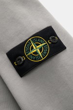 Close-up front-side view of Stone Island Hoodie grey showing black patch with green and yellow compass logo and branded buttons on soft, garment-dyed pure cotton fabric.

Description:  
<p>Timeless casualwear: The hoodie by STONE ISLAND is an indispensabl