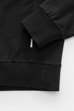 Schwarzer 04651/ A trip in a bag Kapuzenpullover 'IF Hoodie' in Nahaufnahme seitlich mit elastischer Qualität, reiner Baumwolle, kleinem Weblabel.