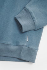 Nahaufnahme des Ärmels vom 04651/ A trip in a bag Kapuzenpullover 'CW Hoodie' rauchblau, Mix aus Wolle und Baumwolle, weicher Griff, Regular Fit, praktische Kapuze, kleines Weblabel in der Seitennaht, komfortable Rippbündchen, fotografiert von oben.