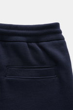 Nahaufnahme der Thom Browne Sweathose navy aus reiner Baumwolle, weicher Griff, elastischer Bund mit Tunnelzug, schmal zulaufend, mit Rückentasche, frontal fotografiert.