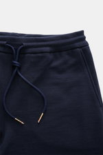 Nahaufnahme der Thom Browne Sweathose navy aus weicher, reiner Baumwolle, slim Fit mit elastischem Bund und markentypischem Streifen-Detail.