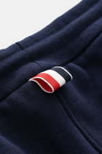 Nahaufnahme der Thom Browne Sweathose navy aus reiner Baumwolle, slim fit mit elastischem Bund und markentypischem Streifen-Detail, seitlich fotografiert.
