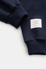 Thom Browne Sweathose navy in Nahaufnahme von oben, weicher Baumwollstoff mit Rippbündchen und weißem Markenlabel sichtbar.