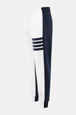 Thom Browne Sweathose weiß/navy, seitlich fotografiert, aus reiner Baumwolle, tapered Fit, elastischer Bund, Streifen-Detail, Rippbündchen, knöchellang, schmal zulaufend.