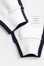 Nahaufnahme der Thom Browne Sweathose weiß/navy von unten schräg, zeigt weichen Baumwollstoff, elastischen Bund, Rippbündchen und markentypisches Patch.