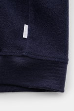 Close-up of the hem of the 04651/ A trip in a bag Blouson dunkelblau, showing its soft wool-cotton fleece texture, ribbed cuffs, and side seam web label, photographed from a front angle.

Description (integrated content): Lässig durch die Übergangszeit: D