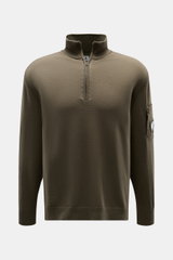 C.P. Company Troyer oliv aus weicher Schurwolle mit Troyer-Kragen, Zipper-Tasche am Oberarm und Linsen-Detail, frontale Nahaufnahme.