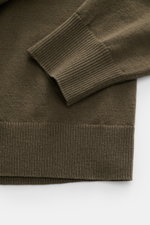 Nahaufnahme des C.P. Company Troyer oliv von oben, zeigt weiche Schurwolle, flexible Rippbündchen und feine Strickstruktur.