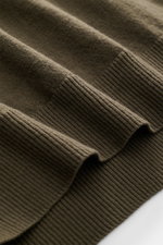 Nahaufnahme des olivfarbenen C.P. Company Troyer, Detailansicht des weichen Schurwollstoffs mit Rippbündchen, seitliche Perspektive.