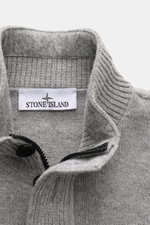 Stone Island Half-zip jumper 'Lambswool' grey melange shown from a close-up top front view, featuring a half-zip collar with embossed buttons, knitted wool blend with soft medium-fine knit, ribbed bands, contrasting knit stripes, and the signature compass