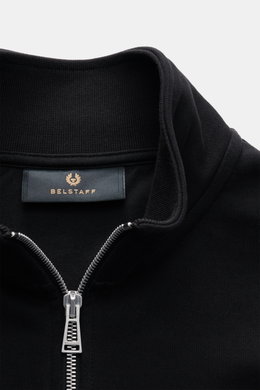 Close-up front view of Belstaff Sweat half-zip jumper 'Quarter Zip' black showing half-zip collar, BELSTAFF woven label on chest, sweat fabric made of cotton, soft feel, slim fit, and flexible ribbed bands.
