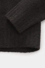Nahaufnahme des breiten Rippbündchens vom 04651/ A trip in a bag Troyer 'Cloudy Wool' dunkelbraun meliert, Regular Fit, mittelgrobes Strickbild, weicher Griff, Mix aus Schurwolle und Microfaser, Troyer-Kragen mit Knöpfen, fotografiert von schräg oben.