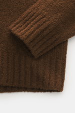 Braunes Detailfoto des 04651/ A trip in a bag Troyer 'Molly' in Bouclé-Struktur mit weichem, voluminösem Griff und Rippbündchen, Nahaufnahme.