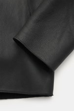 Emporio Armani Black sheepskin jacket close-up from the side showing supple lamb suede leather, sheepskin lining, regular fit, two-way zipper, practical hood, and side pockets.