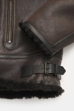 Nahaufnahme der braunen Belstaff Lammfelljacke 'Buxton Phoenix' mit edlem Lammfell, Rindslederbesatz, robustem Reißverschluss und variablen Details aus seitlicher Perspektive.
