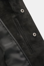 Close-up of the Tom Ford Velourslederjacke schwarz, showing the soft black suede material, snap buttons with logo, and sleek pocket detail from a top-down angle.