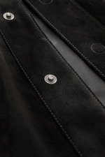Close-up view of the Tom Ford Velourslederjacke schwarz showing fine black suede leather, detailed stitching, and branded metal snap buttons, photographed from a top angle. <div class="relative w-full overflow-visible">
<section class="text-token-text-pr