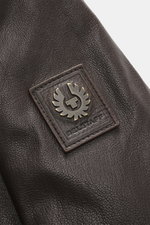 Nahaufnahme des Belstaff Lederblouson 'Winchester Jacket' dunkelbraun mit robustem Ziegenleder und aufgenähtem Logo, Detail von der Ärmelaußenseite.