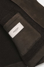 Nahaufnahme der Innenseite der Agnona Velourslederjacke dunkelbraun mit softem Shearling-Futter und Label, Detailansicht aus schräger Perspektive.