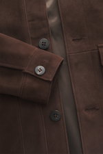 Nahaufnahme der dunkelbraunen 04651/ A trip in a bag Nubuklederjacke 'Workwear Jacket' aus feinem Lammleder, zeigt weichen Griff, Knöpfe, Umlegekragen und aufgesetzte Taschen.