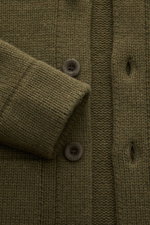 Nahaufnahme des olivfarbenen 04651/ A trip in a bag Cardigan 'Boiled Blouson' mit weichem Woll-Mix, sechs Knöpfen, Rippbündchen und mittelfeinem Strickbild, fotografiert von oben.