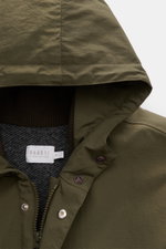 Nahaufnahme des olivgrünen 04651/ A trip in a bag Parka 'The Triple' mit Kapuze, Reißverschluss, Knöpfen und kontrastierendem Innenfutter.