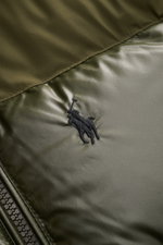 Nahaufnahme der glänzenden Oberfläche und des dezenten Stick-Logos der Polo Ralph Lauren Daunenjacke oliv aus recycelter Microfaser.