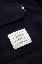 Nahaufnahme der navy Thom Browne Jacke, Fokus auf das Baumwollmaterial mit Label und markanten Streifen am Ärmel, seitliche Perspektive.