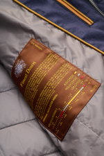 Close-up interior view of the Moorer Down jacket 'Zavyer' navy mottled showing a brown label with yellow text detailing finest down insulation and thermal index, smooth lining, and quilted stitching. The elegant quilted jacket 'Zavyer' by MOORER will see 