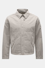 Stone Island Jacke 'Ghost Piece' hellgrau, frontal fotografiert, Slim Fit, Microfaser, Druckknopfleiste, Umlegekragen, Fronttaschen, Kompass-Badge, Ärmel mit Druckknopf.