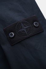 Nahaufnahme des schwarzen Logos auf dem Ärmel der Stone Island Jacke „All-Weather S.I. Ghost Piece“ navy aus dicht gewebtem Baumwollcanvas.