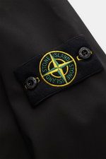 Close-up view of the Stone Island Blouson 'Light Soft Shell-R' black showing the embroidered compass badge on the upper sleeve, highlighting its high-quality microfibre material and smooth texture. Style meets function with wind and water repellent featur