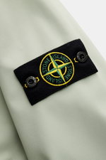 Close-up view of the Stone Island Blouson 'Light Soft Shell-R' salbei showing the black compass badge with yellow and green embroidery on the soft shell fabric. Stil trifft Funktion: Die Soft Shell Jacke von STONE ISLAND überzeugt mit sportivem Design sow