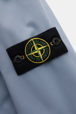 Close-up side view of Stone Island Jacke 'Light Soft Shell-R' rauchblau showing the black compass badge on smooth, high-quality microfiber fabric.

<p>Stil trifft Funktion: Die Soft Shell Jacke von STONE ISLAND überzeugt mit sportivem Design sowie einem d