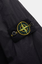 Close-up side view of Stone Island Jacket 'Garment Dyed Crinkle Reps NY' dark navy showing the black compass badge with yellow and green embroidery on lightweight creased microfibre fabric.