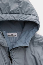 Close-up front view of Stone Island Blouson 'Garment Dyed Crinkle Reps NY' rauchblau in lightweight microfaser with crinkle effect, zippered collar, and padded hood. Funktion trifft Style: Der sportive Blouson von STONE ISLAND besteht aus einem leichten M