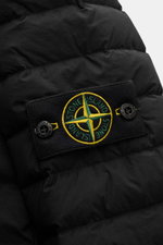 Close-up front view of Stone Island Daunenjacke 'Seamless Tunnel Nylon Down-TC' schwarz showing black puffer fabric and iconic compass badge with buttons.