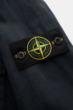Close-up side view of Stone Island Blouson 'Stretch Cotton Twill-TC' navy showing the embroidered logo patch with buttons on elastic cotton fabric. Sportives Frühlings-Essential: Mit seinem leichten Baumwollmaterial wird der STONE ISLAND Blouson zum ideal