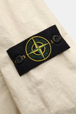 Close-up front perspective of Stone Island Jacket 'Membrana' cream showing textured cream fabric and black patch with yellow-green compass badge and buttons.

Function meets style: The triple-layer functional fabric of this STONE ISLAND jacket is laminate