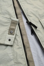 Nahaufnahme der Stone Island Jacke 'Membrana' salbei, zeigt Reißverschluss, Ärmel mit Knopf, hochwertiges, wind- und wasserabweisendes Funktionsgewebe.