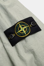 Nahaufnahme der Stone Island Jacke 'Membrana' salbei am Ärmel mit dem schwarzen Kompass-Badge, hochwertiges, leicht griffiges, wind- und wasserabweisendes dreilagiges Funktionsgewebe.